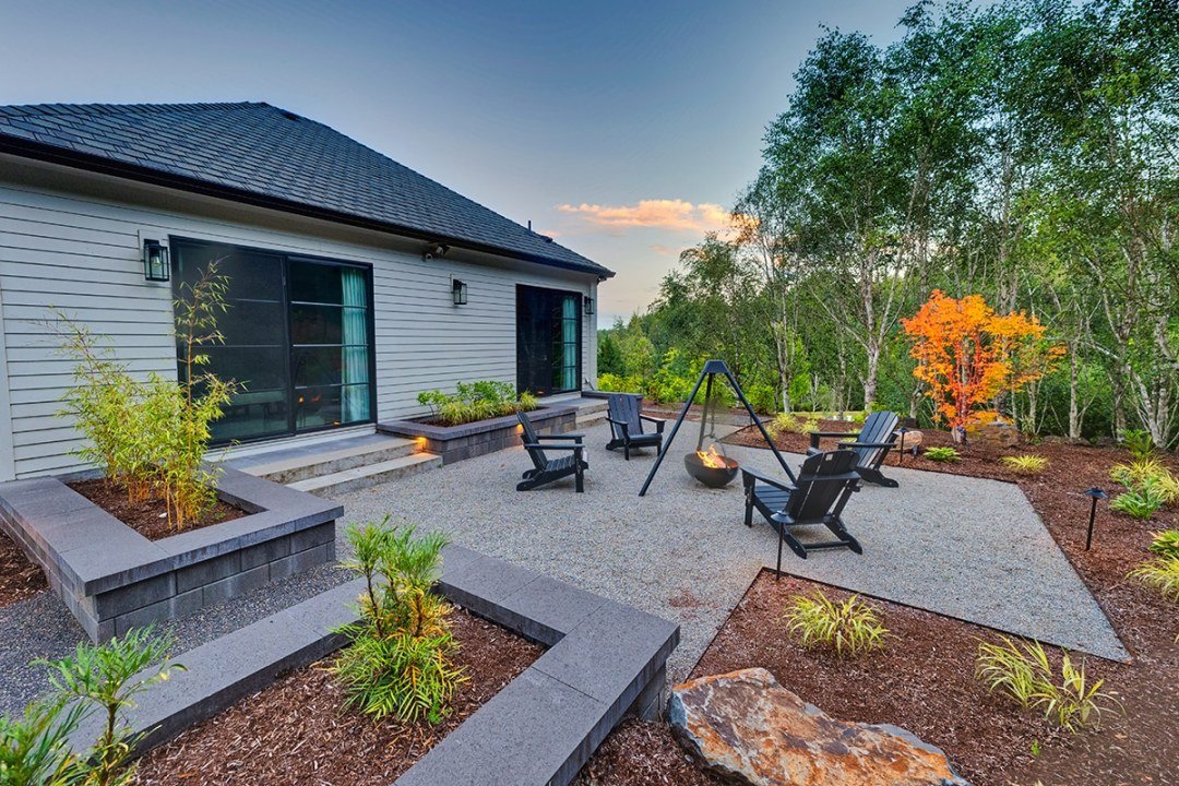 A fire pit in a cauldron surrounded by chairs on a gravel square in front of a house - Dennis' 7 Dees Landscaping in Portland