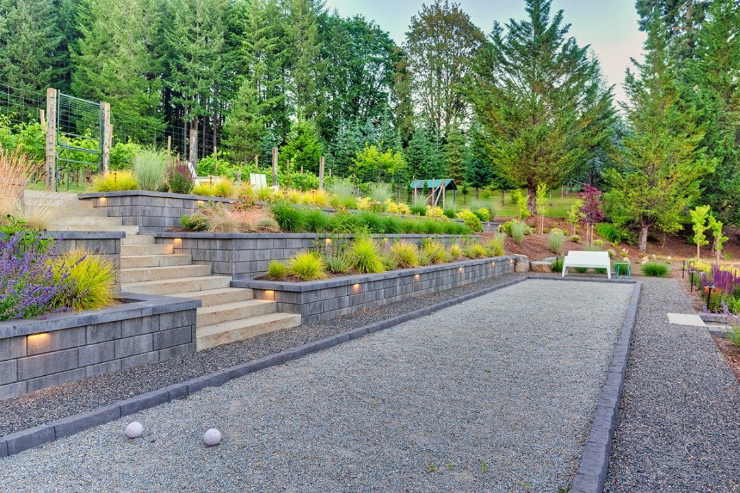Bocce ball court on a sloped yard with retaining walls and plantings by 7 Dees Landscaping