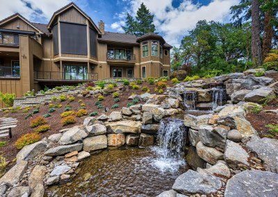 Natural stone waterfall water feature designed on a sloped landscape by Dennis' 7 Dees