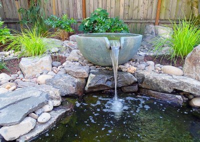 Water feature with large bowl pouring into small rock-lined pond - 7 Dees Landscaping