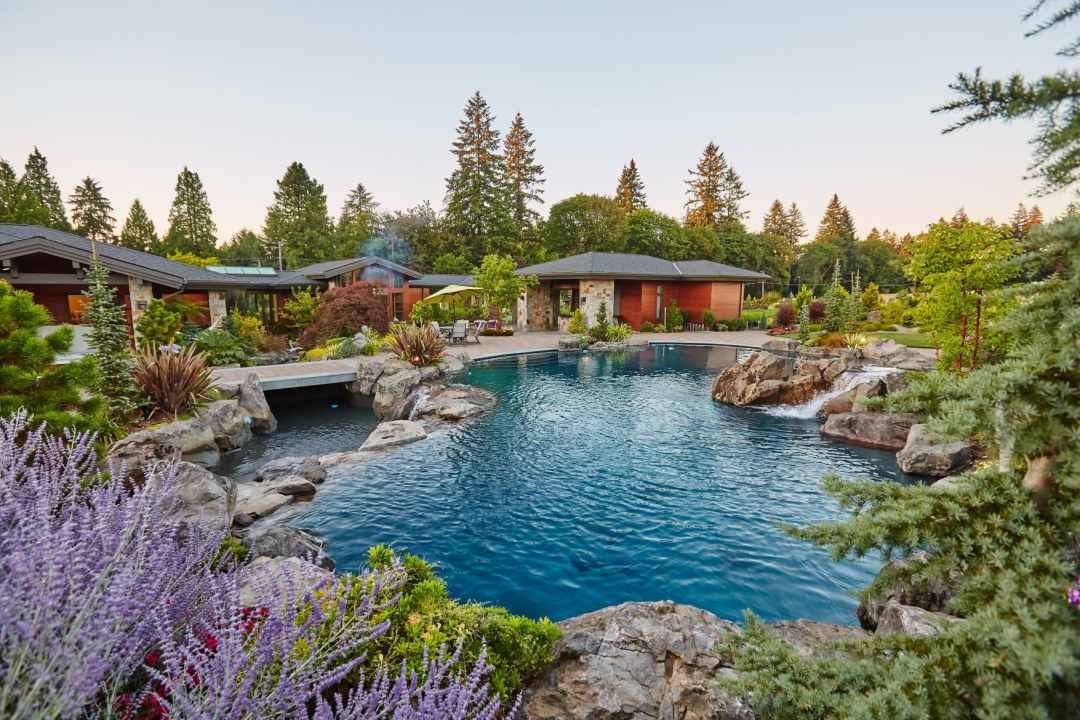 A residential pool with waterfalls, natural stones, and lush PNW plantings